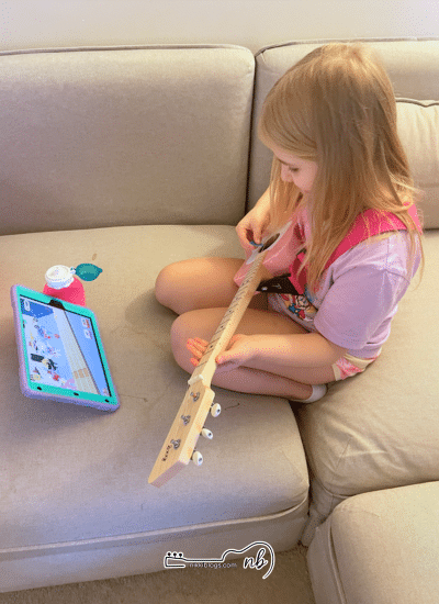 girl playing loog pro guitar with app